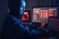 Girl hacker in a hood typing program code while committing a cybercrime hacking a system on the background of screens