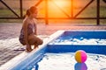 A girl with hair braided in a bun in bright suit plays by the pool with a ball against the background of summer sun Royalty Free Stock Photo