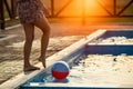 A girl with hair braided in a bun in bright suit plays by the pool with a ball against the background of summer sun Royalty Free Stock Photo