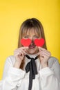 Girl with half smile with two small red hearts in the hands under the eyes on yellow background. Valentine`s Day Royalty Free Stock Photo