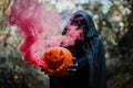 Girl with halloween costume and make up, holding a pumpkin with a smoke bomb inside - Holidays, party, scary and autumn concept -