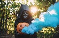 Girl with halloween costume and make up, holding a pumpkin with a smoke bomb inside - Holidays, party, scary and autumn concept -
