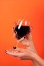 Girl hand with black nail holding glass of wine isolated on orange background Royalty Free Stock Photo