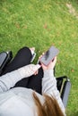 Girl with a hand and a foot bandaged in a wheelchair. Mobile phone screen in black on green grass