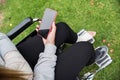 Girl with a hand and a foot bandaged in a wheelchair. Mobile phone screen in black on green grass