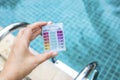 Girl hand holding mini water testing test kit over blurred swimming pool background