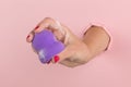 Girl hand holds a beauty blender for makeup from a hole in a pink background, copy space. Sponge in soapy foam, how to clean Royalty Free Stock Photo