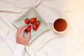 Girl hand picking strawberries. Cozy scene at home, tea cup in blanket Royalty Free Stock Photo