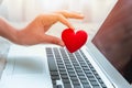 Girl hand take red heart at laptop keyboard for social online love chat and sharing encouragement over internet to fight Covid-19