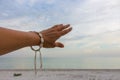 Girl hand touching the sky on calm sea background. Hand with bracelet from shells on beach background. Tranquility concept.