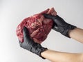 Girl hands dressed in black gloves holding a large piece of fresh raw beef on a light background