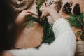 Girl hands holding fir branches and pine cones, thread, scissors on wooden table. Making rustic christmas wreath. Details for Royalty Free Stock Photo