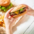 Girl hands holding fresh tasty burger and french fries, sauce on the wooden plate, white table. Top view. Flat lay Royalty Free Stock Photo