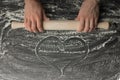 Girl hands holding a rolling pin with flour on a dark black table, with a heart made of flour Royalty Free Stock Photo