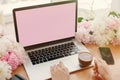 Girl hands on stylish laptop with empty screen and coffee, phone, black notebook and peonies on rustic wooden table. Freelance Royalty Free Stock Photo