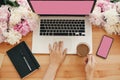 Girl hands on stylish laptop with empty screen and coffee, phone, black notebook and peonies on rustic wooden table. Freelance Royalty Free Stock Photo