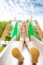 Girl with hands up sits on playground chute