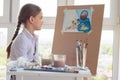 The girl happily looks at her finished drawing hanging on an easel