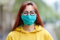 A girl with happy eyes, glasses in a reusable blue medical mask stands straight and looks straight