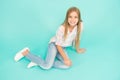 Girl happy face sit on floor attentive looking at camera turquoise background. Kid girl with long hair relaxing. Just