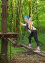 Girl in harness crossing rope bridge in forest
