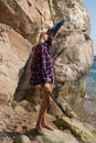 Girl with harpoon in flannel shirt on the rocky beach Royalty Free Stock Photo