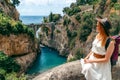 A girl in a hat with a backpack enjoys an incredibly beautiful view of a stone bridge over the gorge Fiordo di Furore. Little bay