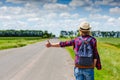 Girl with hat and backpack hitchhiking on the road Royalty Free Stock Photo