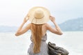 Girl in a hat with a backpack sitting on the pier. Mountains on the background. View from the back Royalty Free Stock Photo