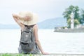 Girl in a hat with a backpack sitting on the pier. Mountains and Royalty Free Stock Photo