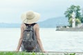 Girl in a hat with a backpack sitting on the pier. Mountains and lighthouse on the background Royalty Free Stock Photo