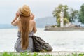 Girl in a hat with a backpack sitting on the pier. Mountains and lighthouse on the background. View from the back Royalty Free Stock Photo