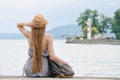 Girl in a hat with a backpack sitting on the pier. Mountains and lighthouse on the background. Royalty Free Stock Photo