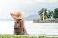 Girl in a hat with a backpack sitting on the pier. Mountains and lighthouse on the background. View from the back Royalty Free Stock Photo