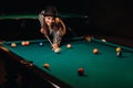A girl in a hat in a billiard club with a cue in her hands hits a ball.Playing pool Royalty Free Stock Photo