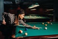 A girl in a hat in a billiard club with a cue in her hands hits a ball.Playing pool Royalty Free Stock Photo