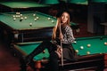 A girl in a hat in a billiard club sits on a billiard table with a cue in her hands.Playing billiards Royalty Free Stock Photo