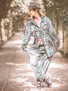 A girl in a hat and a careless oversized outfit stands in a curtsy pose on an alley in the park. Street dancer Royalty Free Stock Photo