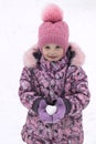 Girl in hat, coat and mittens holding a snowball in the shape of a heart.