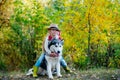 Girl in hat hugging her dog. Little girl with her dog, alaskan malamute, full length. Child and dog on nature background Royalty Free Stock Photo