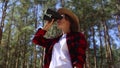 Girl in a hat looks through binoculars in the forest. Concept hike, tourism.