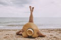 Girl in hat lying on beach with legs up. Fashionable young woman covering with straw hat, relaxing on sandy beach near sea. Summer Royalty Free Stock Photo