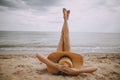 Girl in hat lying on beach with legs up. Fashionable young woman covering with straw hat, relaxing on sandy beach near sea. Summer Royalty Free Stock Photo