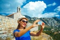 Girl in the hat making selfie by the smartphone on the background of the church in the mountains Royalty Free Stock Photo