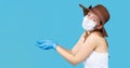 A girl in a hat and a medical mask looks at the camera and stretches her arms to the side. Fighting the spread of the virus and