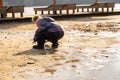 girl in a hat and overalls poking around in the mud near a large dirty pool