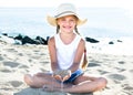 Baby girl in hat playing with sand on sea coast in summer