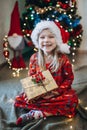 A girl in a hat of santa claus sorts out gifts against the background of a Christmas tree Royalty Free Stock Photo