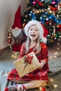 A girl in a hat of santa claus sorts out gifts against the background of a Christmas tree Royalty Free Stock Photo