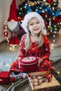 A girl in a hat of santa claus sorts out gifts against the background of a Christmas tree Royalty Free Stock Photo